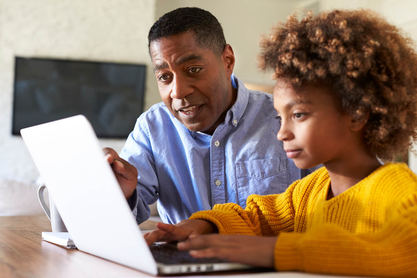 Male teacher sitting with student looking at laptop in a classroom.