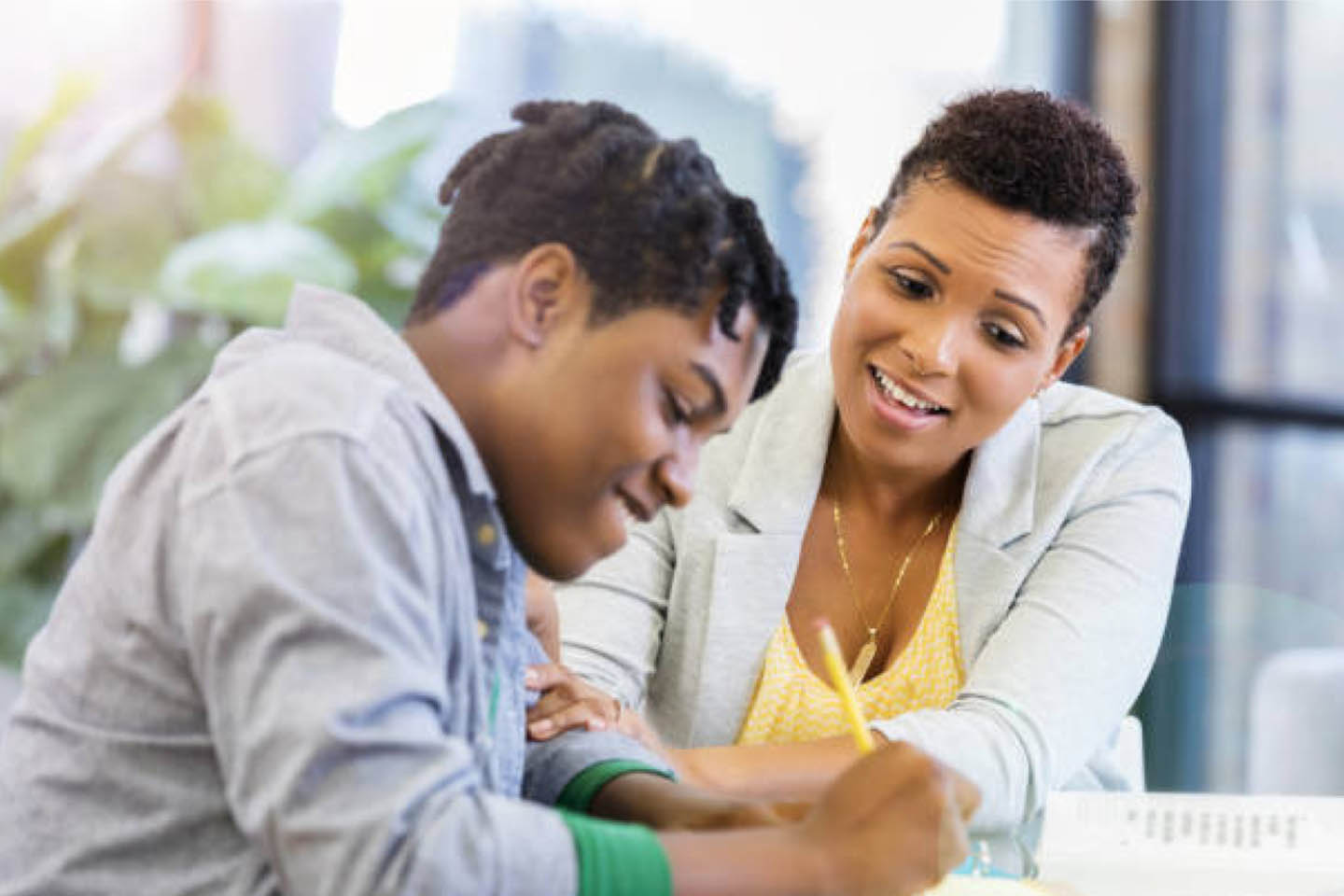 Black female teacher helping a Black middle school student with his school curriculum work.