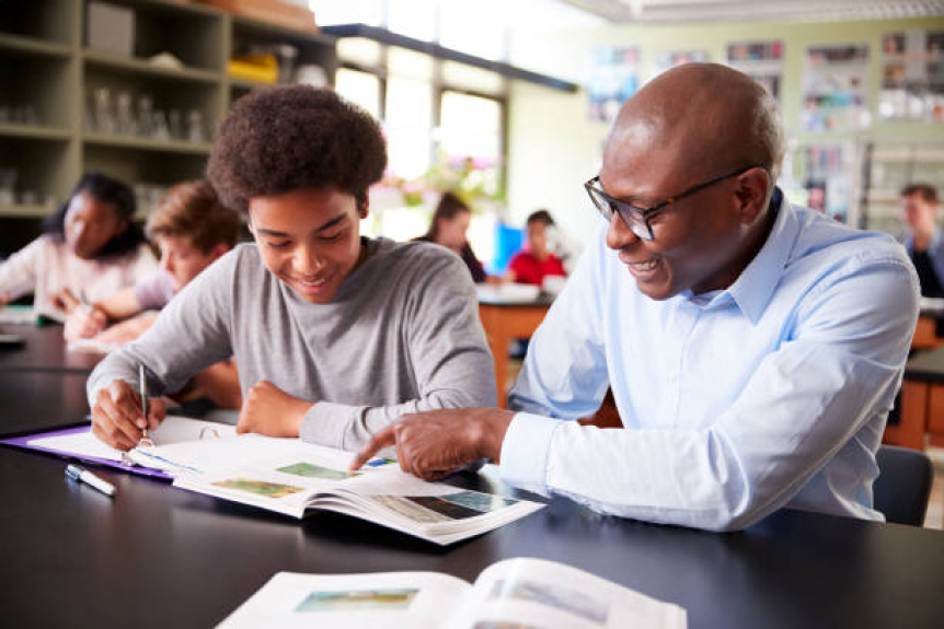 Black male educator tutoring a Black male high school student in a classroom.