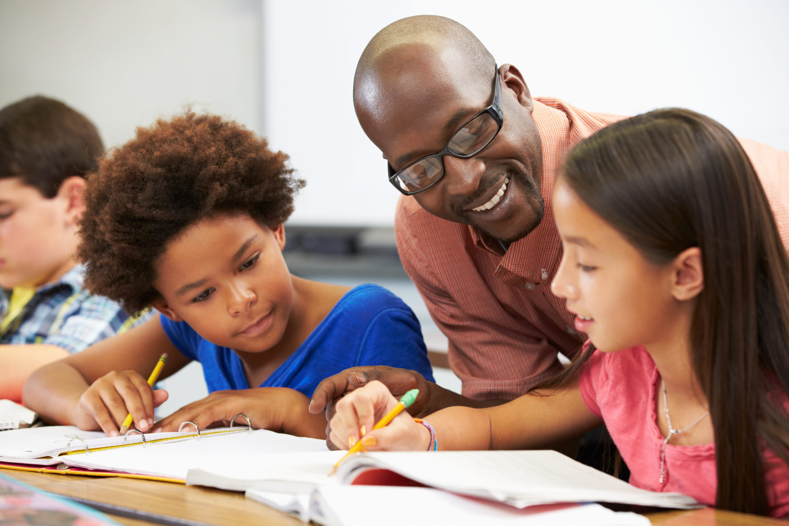 Black male teacher helping MLL students with curriculum in a classroom.
