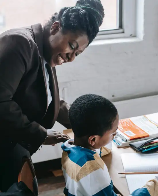Professional Black female school leader interacting with a younger student who is learning in a classroom.