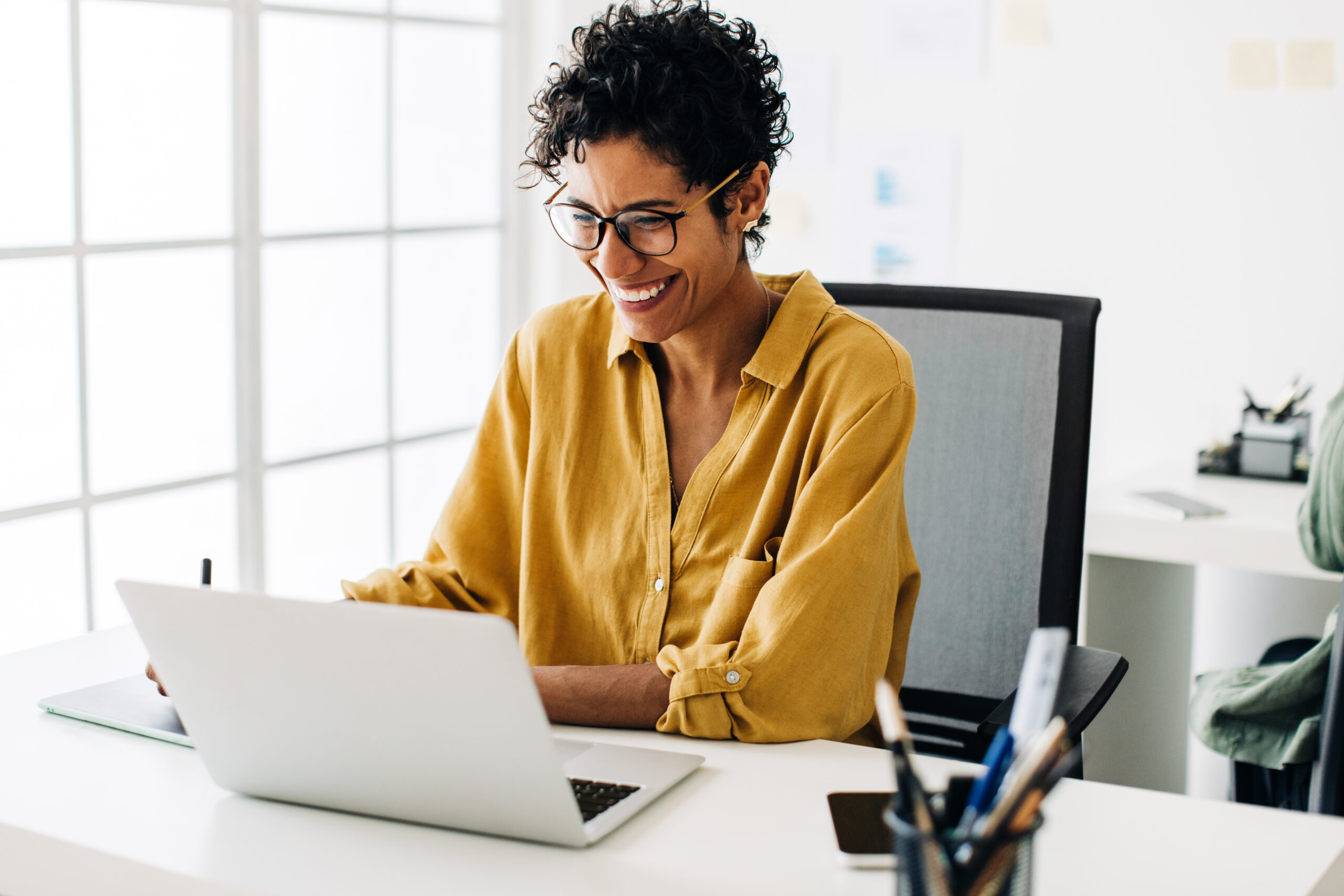 A Black middle-aged woman smiling while analyzing instructional materials data on her computer in her offic.