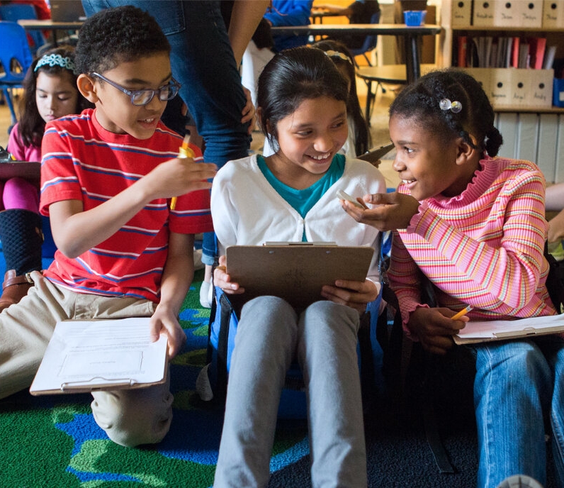 Group of elementary school students sitting and talking collaboratively in a classroom setting.