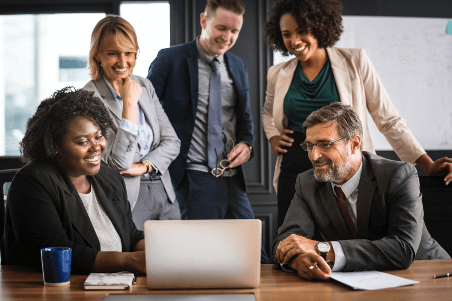 A group of five diverse district leaders in California collaborating and looking at a computer on a table.