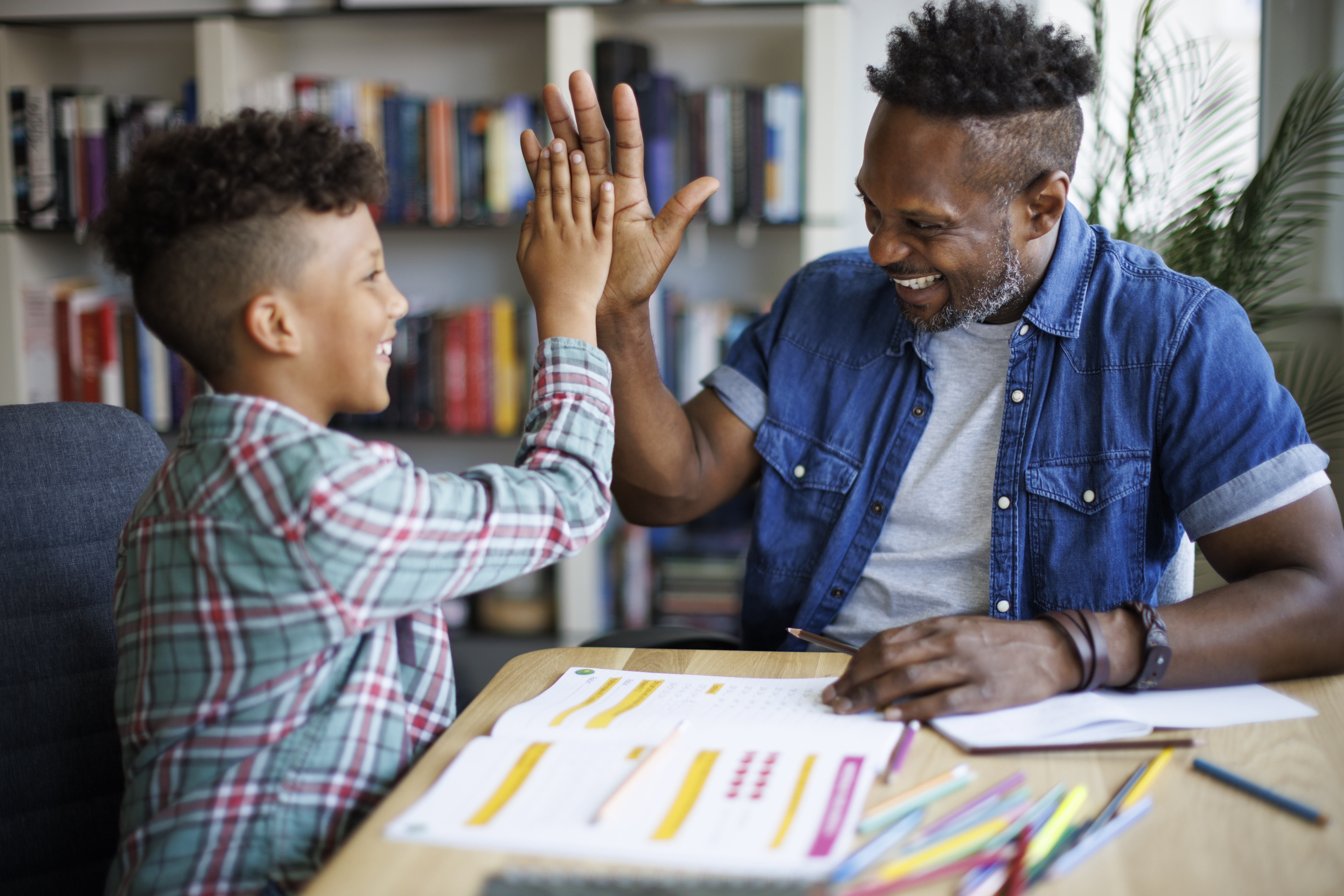 Black male math teacher and student high fiving while working in the library.
