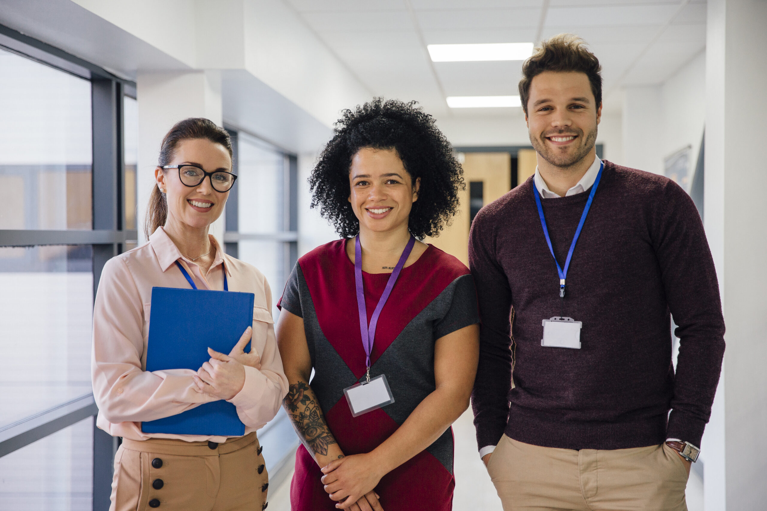 Three diverse principals smiling in a K12 school hallway.