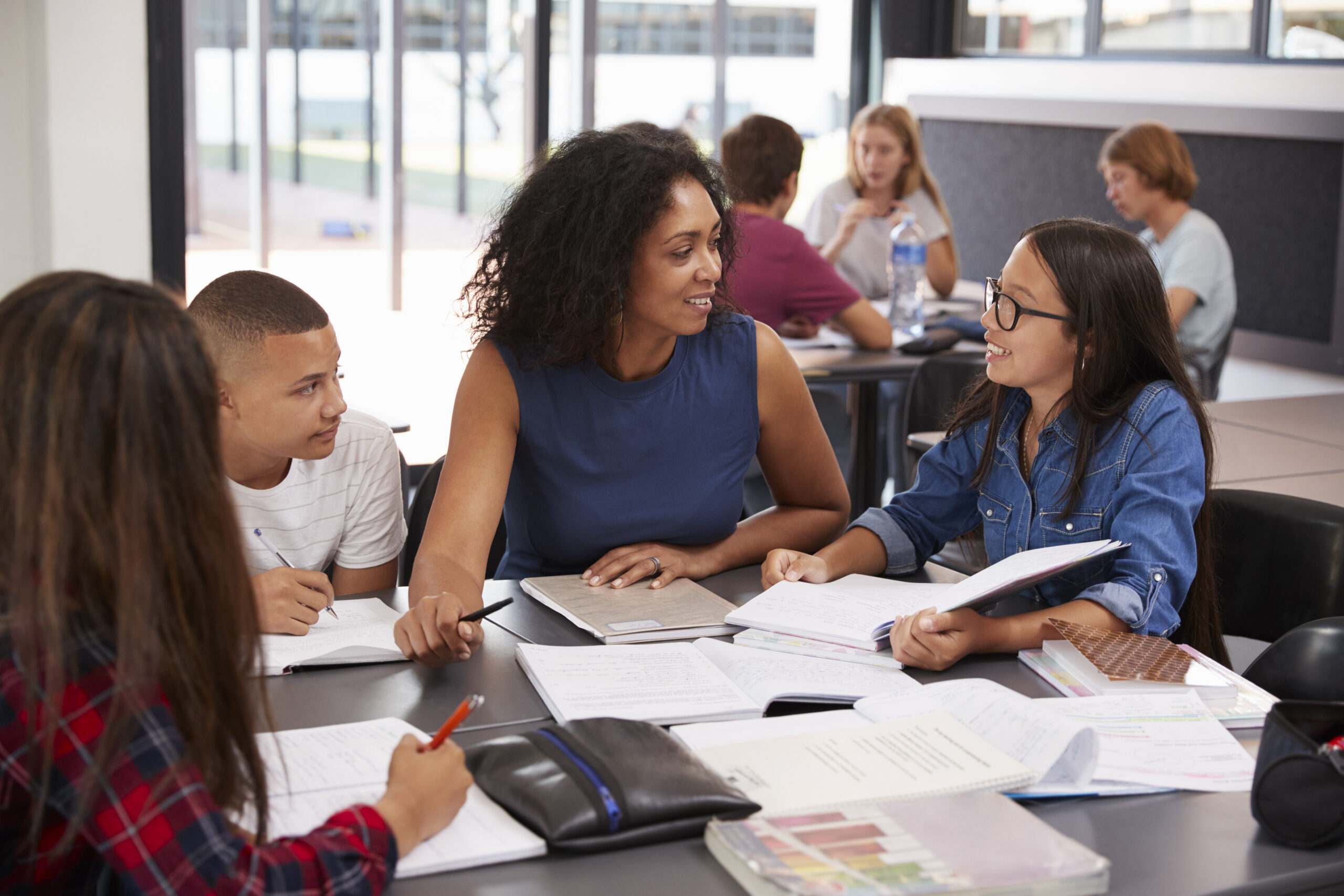 A female African American teacher happily working with a small group of diverse middle school students using HQIM in a classroom.